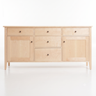 A light natural maple wood sideboard or dresser with four drawers and two cabinet doors, accented by small round dark knobs, shown on a clean white background.