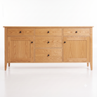 A light oak wood sideboard or credenza with four drawers and two cabinet doors, accented by small round black knobs and supported by tapered legs, shown against a plain white background.